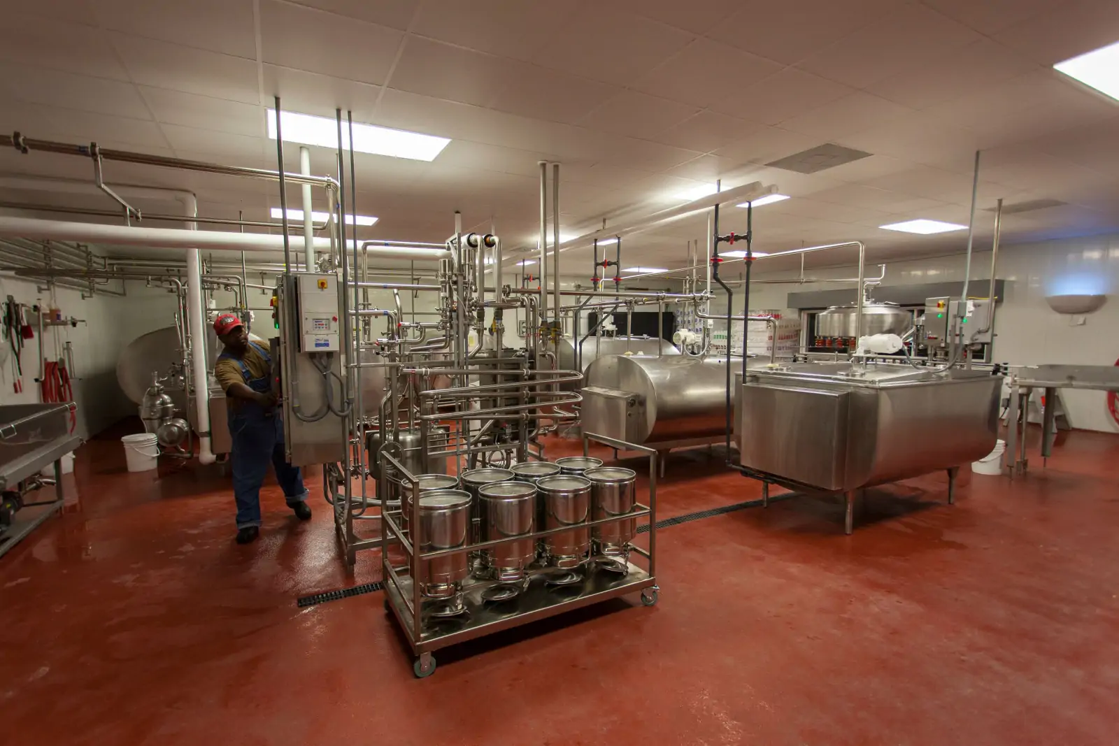Dairy processing hall with stainless-steel tanks, pipework and an operator on the floor