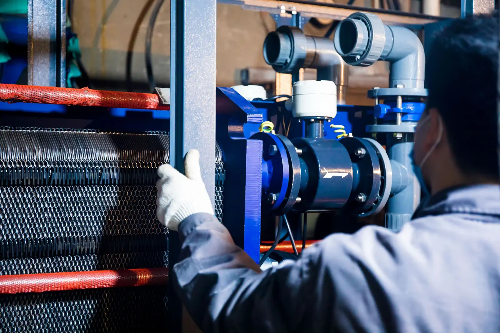 Engineer in gloves working on a pump and plate heat exchanger assembly